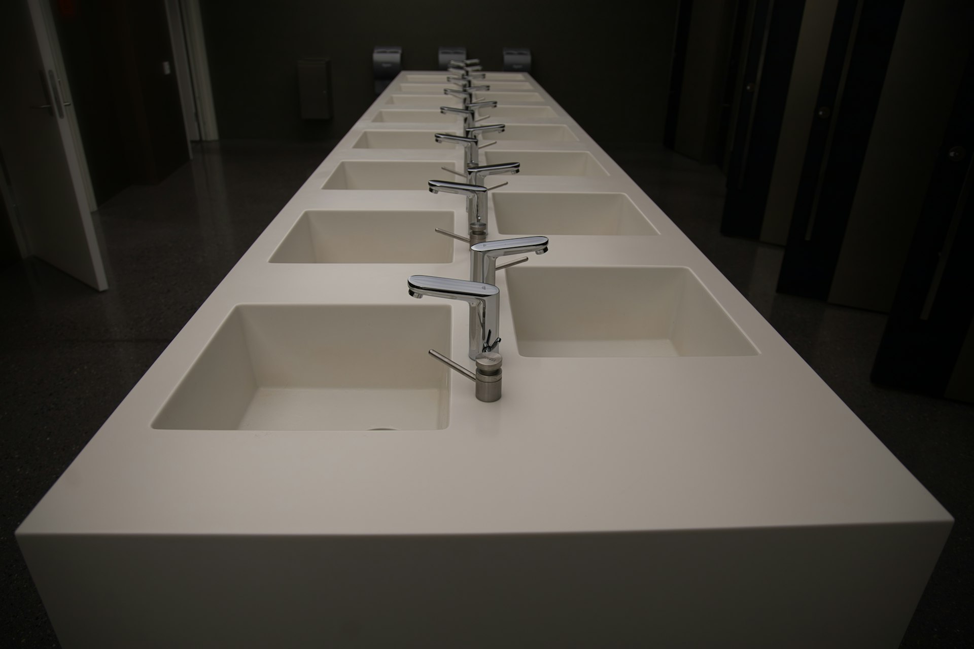 Modern bathroom sinks with sleek, square basins and polished faucets arranged in a row, designed for high-traffic areas.